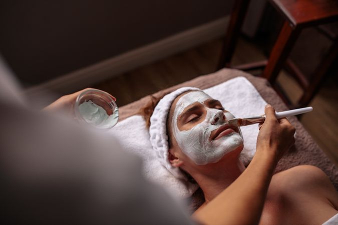 Cosmetician applying facial mask on female face