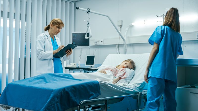 Sick Little Girl Lies on a Bed In the Hospital, Friendly Doctor Writes Medical Record/ Data into Clipboard, Talks with Nurse