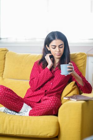 Vertical composition of woman sipping tea on yellow sofa at home