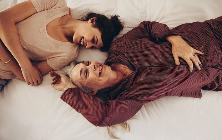 Mother and daughter on bed talking while sleeping in opposite direction facing each other