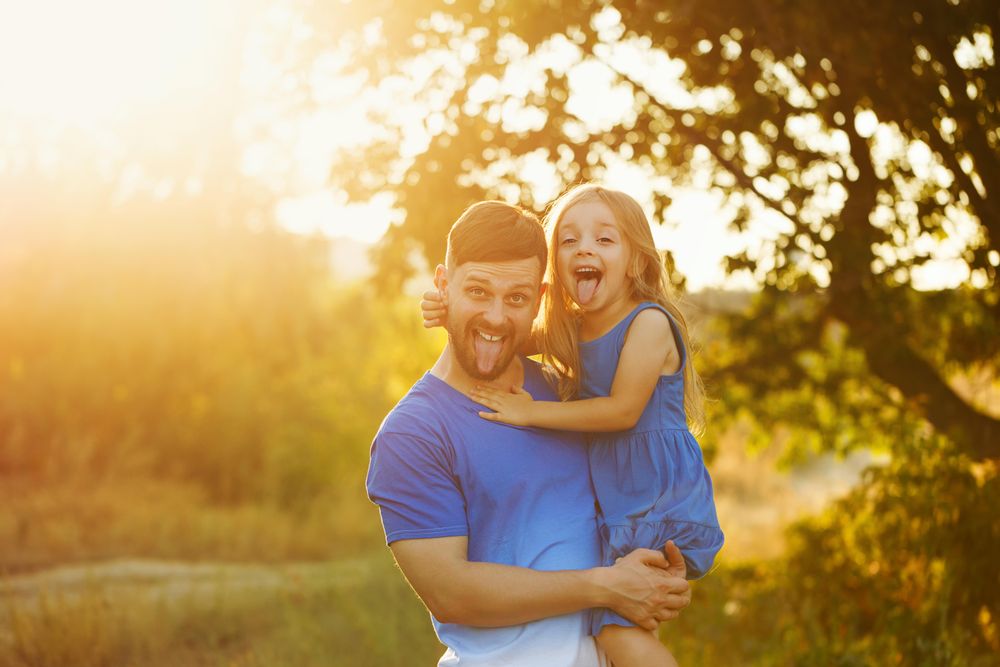 Man with daughter in sunny meadow making funny face