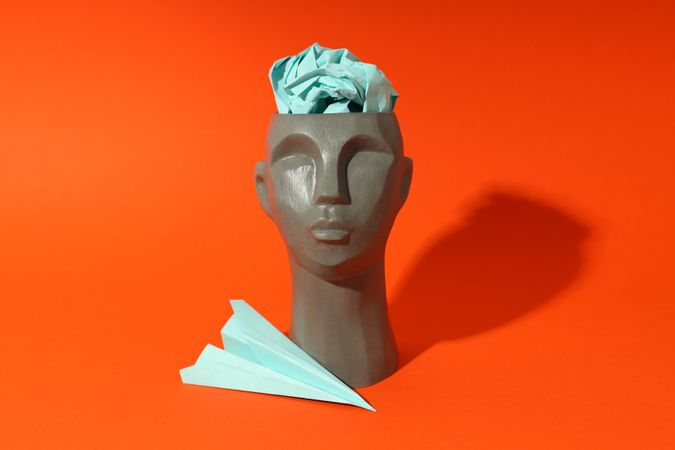 Grey bust of head on red background with paper airplane