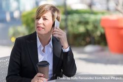 Woman sitting on table outside with coffee speaking on cell phone bDrLy5