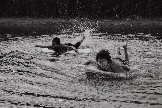 Happy boys swimming with board over water