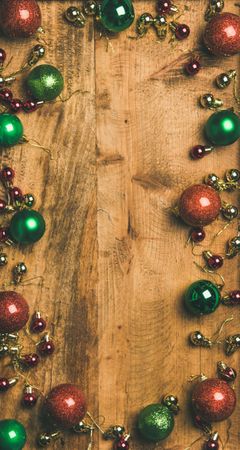Tree ornaments arranged on wooden board, large and small red, green and gold baubles, copy space