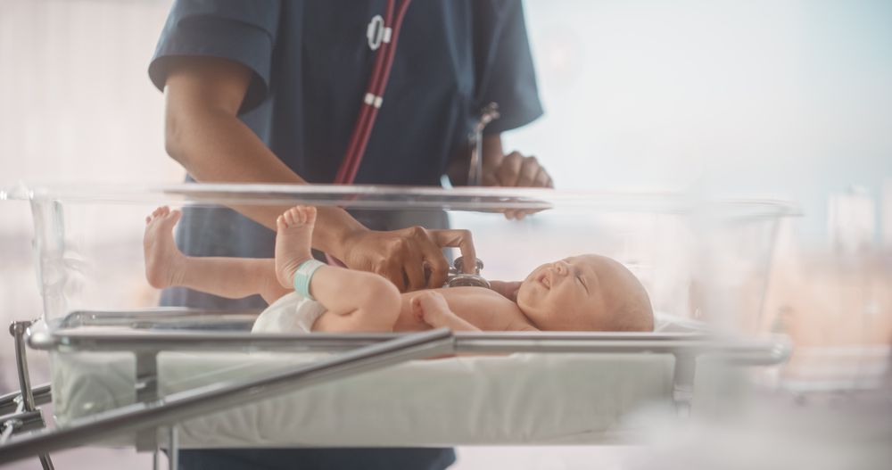 Female Pediatrician Uses Stethoscope to Listen to Heartbeat and Lungs of Recovering Newborn Baby Resting in Bassinet.