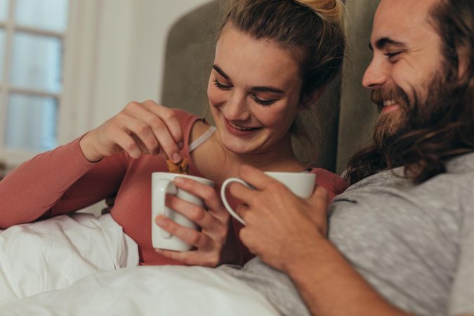 Smiling man and woman with their coffee cups sitting on bed