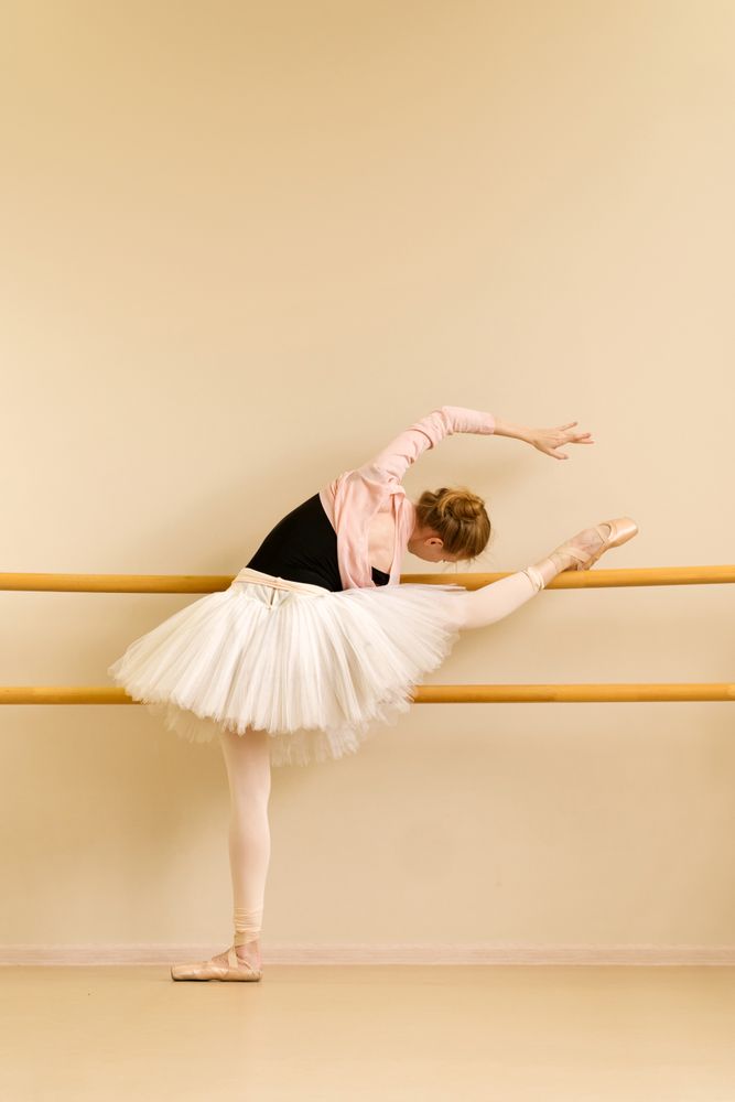 Ballerina performing deep leg stretch at barre during practice.
