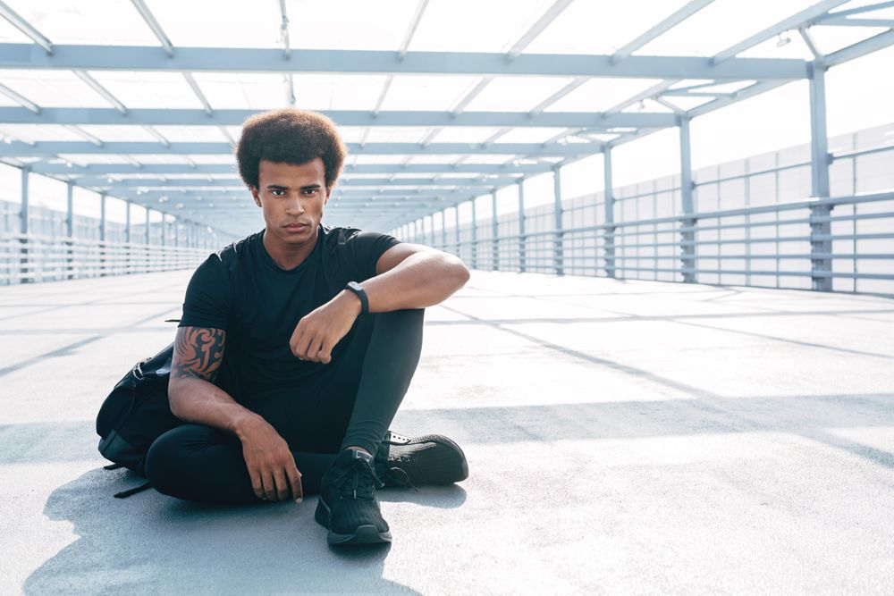 Serious Black sitting on bridge in dark clothes