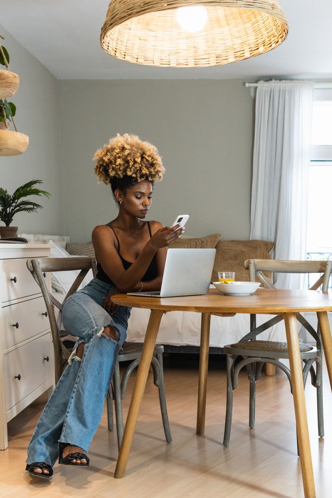 Black woman with laptop and mobile phone sitting on chair during breakfast