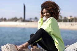 Happy female sitting on rocks near shoreline in bright green shirt