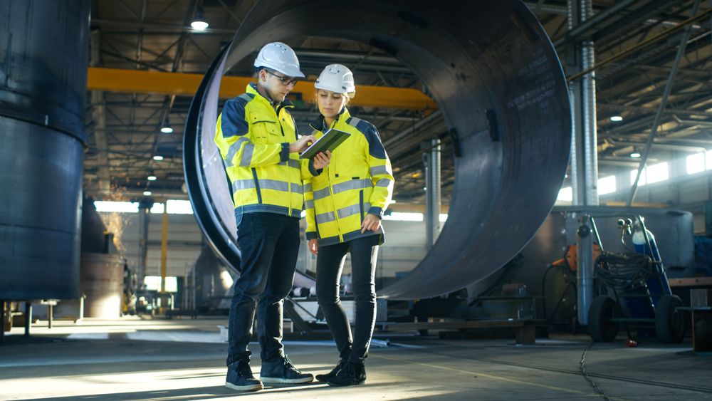Male and Female Industrial Engineers in Hard Hats Discuss New Project while Using Tablet Computer.