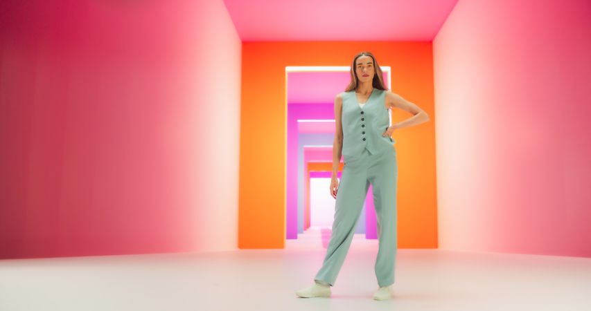 Low Angle Portrait of a Stylish Female Posing Confidently in a Bright Lit Room. Fashionable Young Woman Striking A Pose In Colorful Studio Environment, Working For Luxurious Fashion Brand.
