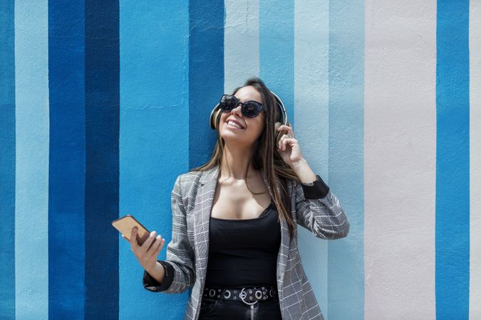 Woman wearing gray blazer and sunglasses listening to music on headphones