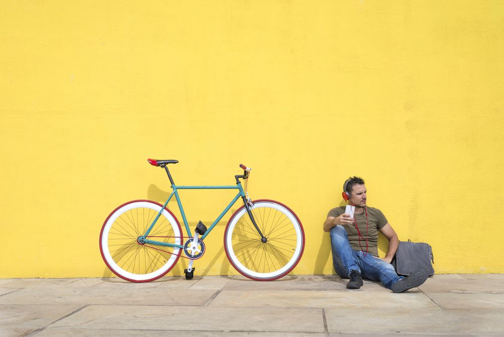 Male sitting in front of yellow wall with bike listening to music