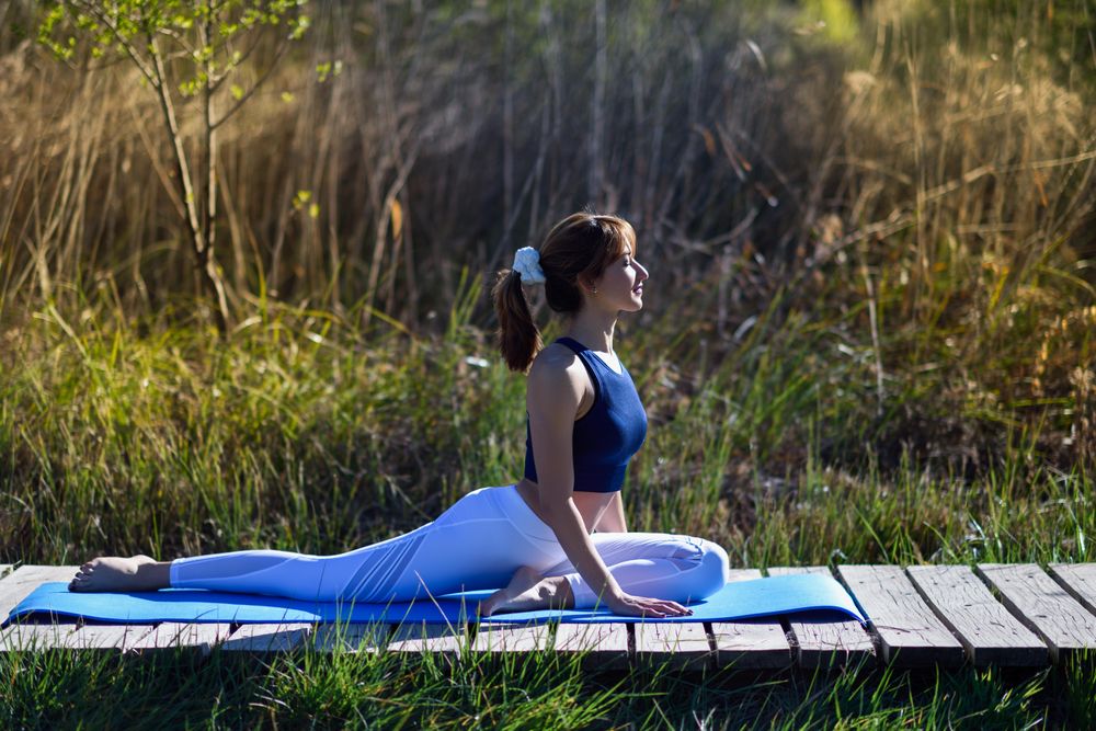 Female wearing sport clothes doing pigeon yoga pose outside
