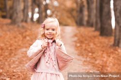 Young girl wearing pink jacket standing on brown tree leaves 48EOXb