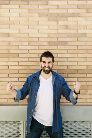 Smiling man clenching fists in celebration in front of brick wall