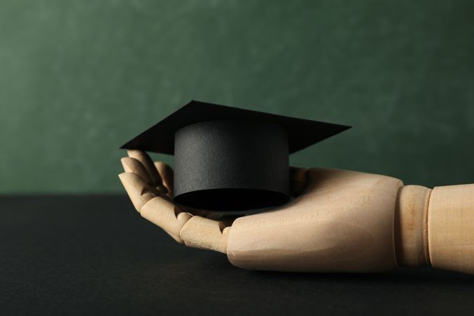 Graduation hat with books on a table on a dark background.