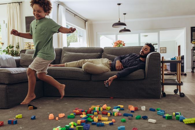 Man sleeping on couch while his kid is playing at home