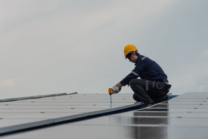 Engineer worker using electric drill repairing on solar cell panel on the roof of the factory. After service and security for industrial renewable energy concept