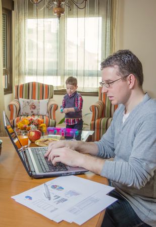 Father working in home office and son playing