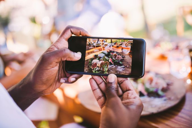 Man photographs a charcuterie board outdoors with a smartphone