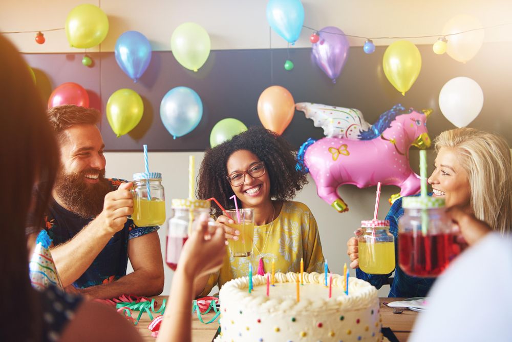 Woman with curly hair in front of a birthday cake toasting drinks with friends