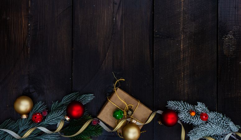 Top view of Christmas gift wrapped in brown paper surrounded by baubles and fir