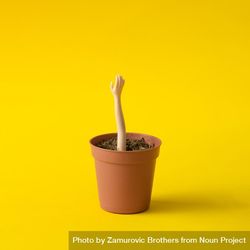 Doll hand reaching out of flower pot on yellow background 0VgmG5