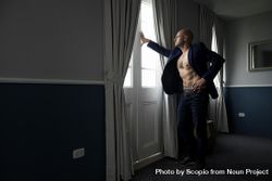 Side view of bare-chested man in blue blazer standing by the window 5zpQob