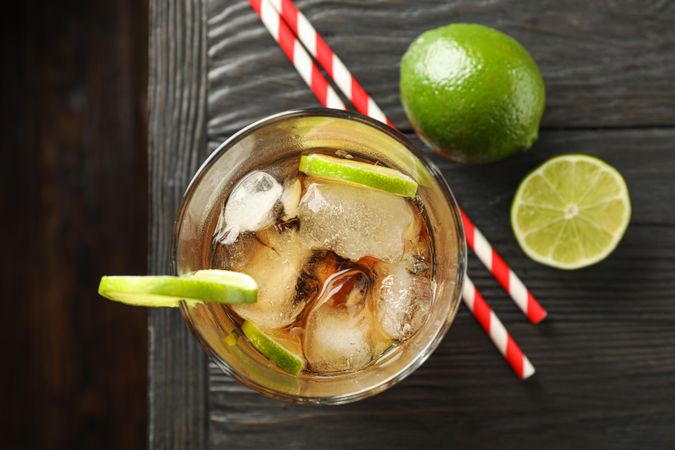 Glass of cold cola with citrus and ice on wooden table, top view