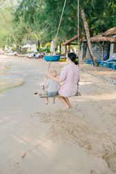 Joyful kid swinging with mother against blurred seascape