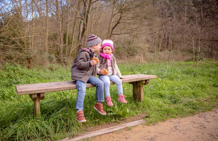 Little boy and girl sitting on park bench talking with snack