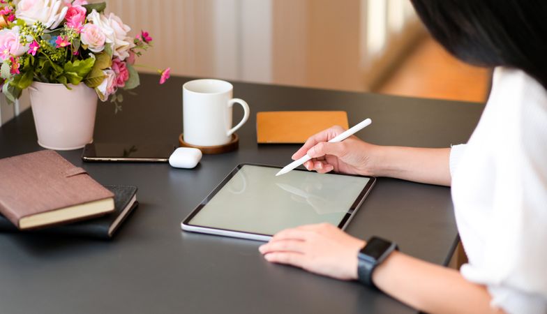 Young women write on modern tablet with a digital pen on a desk with coffee and notebook.