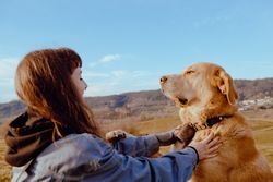 Woman with piercing sitting near dog between field