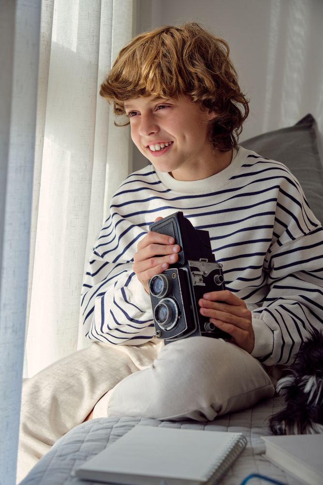 Cheerful boy with retro photo camera on bed