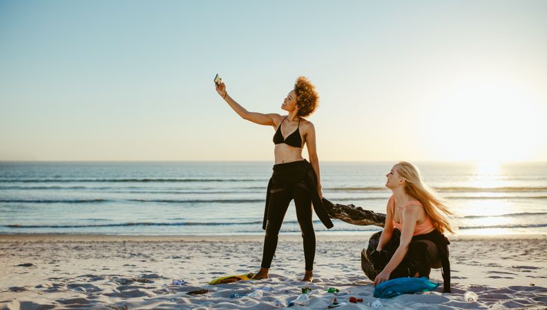 Woman taking selfie with her friend while cleaning the beach area