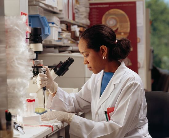 Bethesda, MD - USA, July 2008: A Black female researcher uses pipettes while seated