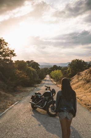Woman standing on road beside motorbike