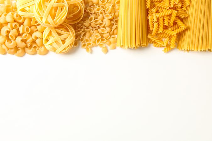 Different pasta on bright background, space for text. Dry uncooked whole pasta