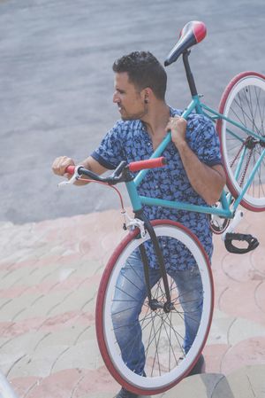 Looking down at male lifting up colorful bike on his shoulders