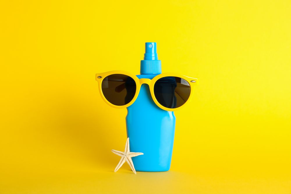 Sunscreen spray with starfish and sunglasses on color background, space for text
