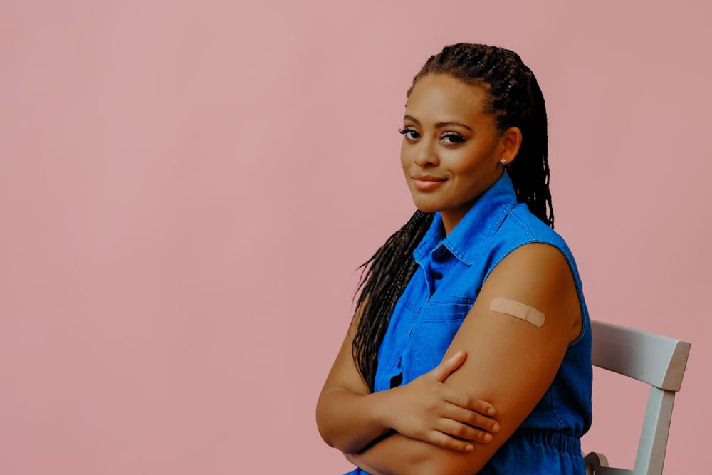 Content female sitting with bandage after immunization in pink studio shoot, copy space
