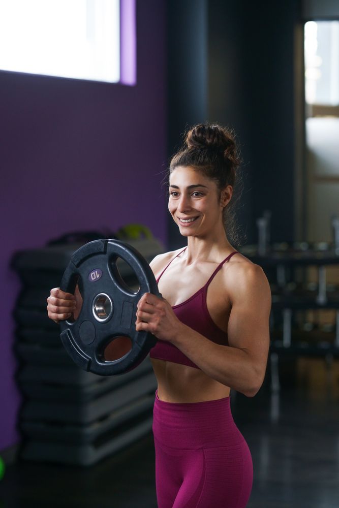 Muscular woman in fitness gear smiling while holding a weight