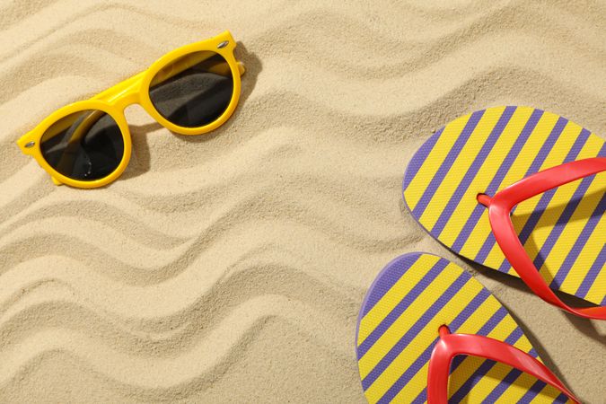 Flip flops and sunglasses on sea sand, space for text