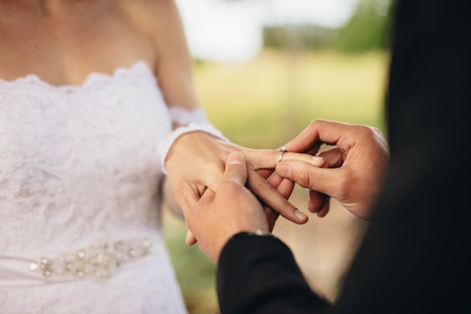 Closeup of couple exchanging wedding rings during their wedding ceremony outdoors