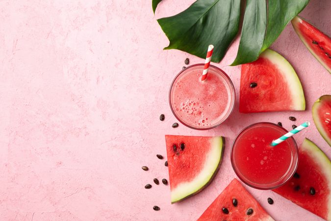Composition with glass of watermelon juice and slices on pink table
