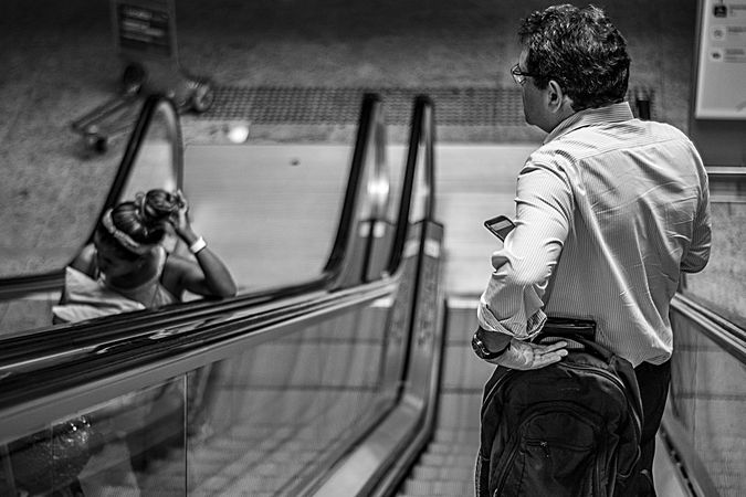 Grayscale photo of young woman and middle aged man on escalator