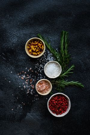 Top view of salt and seasoning bowls and rosemary on kitchen counter, vertical